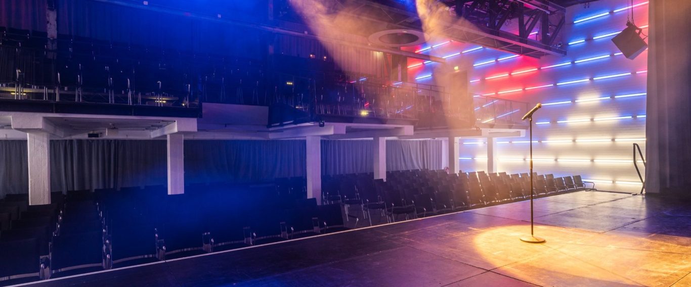 Blick von der Bühne. Leere Reihen von schwarzen Stühlen in einem modernen, bunten Veranstaltungsraum.